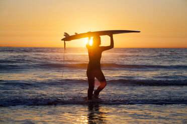 Silhouette female surfer holding surfboard and standing on shore against sky during sunset - CAVF24953