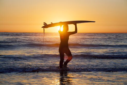 Silhouette einer weiblichen Surferin, die ein Surfbrett hält und am Ufer steht, gegen den Himmel bei Sonnenuntergang - CAVF24953