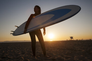 Niedriger Blickwinkel auf eine Frau, die ein Surfbrett hält und am Strand steht - CAVF24955