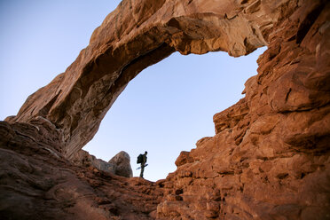 Low angle view of person standing at rock formation against clear sky - CAVF24959