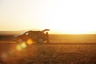 Seitenansicht eines Wanderers, der neben einem Auto auf einem Feld steht, gegen den klaren Himmel bei Sonnenuntergang - CAVF24997