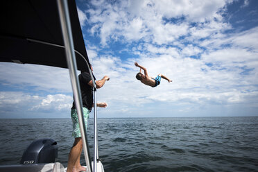 Vater schaut auf seinen Sohn, der gegen den bewölkten Himmel ins Meer springt - CAVF25054