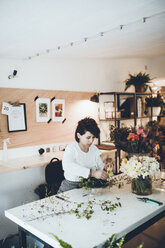 Florist arrangiert Blumen auf Blumenschaum am Tisch im Geschäft - CAVF25094