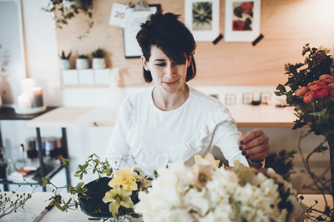 Smiling florist arranging flowers on floral foam at table in store stock photo