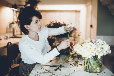 Seitenansicht einer Floristin, die Narzissen in einer Vase im Blumenladen arrangiert - CAVF25098