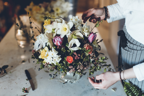 Hochwinkliger Mittelteil eines Floristen, der Blumen arrangiert, während er an einem Tisch im Geschäft steht, lizenzfreies Stockfoto