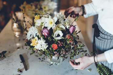 Hochwinkliger Mittelteil eines Floristen, der Blumen arrangiert, während er an einem Tisch im Geschäft steht - CAVF25108