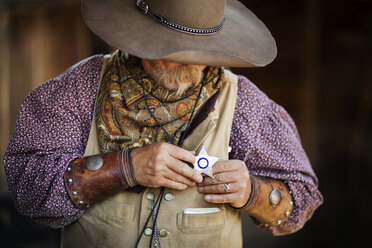 Älterer männlicher Cowboy mit sternförmigem Abzeichen im Stall - CAVF25109