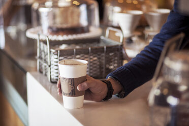 Ausgeschnittenes Bild eines Barista, der einen Einwegbecher am Tresen eines Cafés hält - CAVF25155