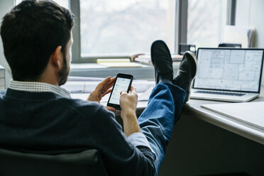 Rückansicht eines Geschäftsmannes, der im Büro sitzt und sein Smartphone benutzt - CAVF25206