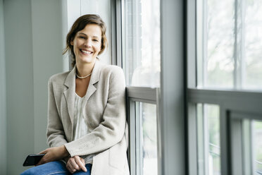 Portrait of smiling businesswoman sitting by window in office - CAVF25216