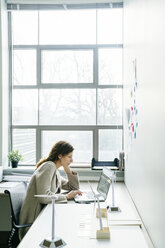 Geschäftsfrau, die einen Laptop benutzt, während sie am Schreibtisch im Büro sitzt - CAVF25219