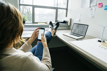 Rückansicht einer Geschäftsfrau, die ein Smartphone benutzt, während sie im Büro sitzt - CAVF25220
