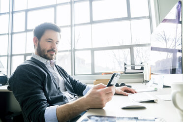 Businessman using smart phone while sitting at desk in office - CAVF25227