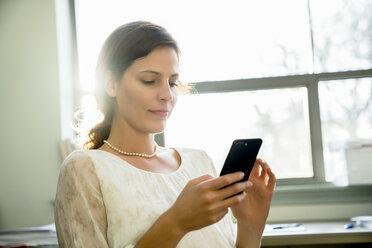 Geschäftsfrau, die im Büro sitzend ein Smartphone benutzt - CAVF25235