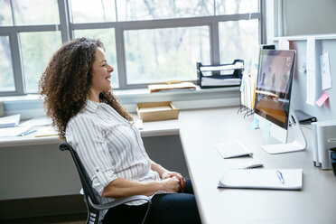 Seitenansicht einer lächelnden Geschäftsfrau mit Blick auf einen Desktop-Computer im Büro - CAVF25238