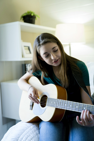 Teenager-Mädchen spielt Gitarre im Schlafzimmer, lizenzfreies Stockfoto