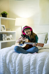 Teenager-Mädchen hört Musik über ihr Smartphone, während sie mit einer Gitarre im Schlafzimmer sitzt - CAVF25326