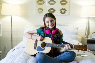 Porträt eines glücklichen Mädchens im Teenageralter, das im Schlafzimmer Gitarre spielt - CAVF25328