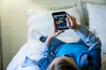 Girl using smart phone while lying on bed at home - CAVF25330