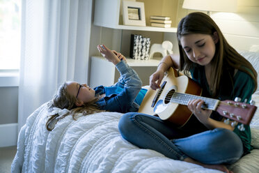 Mädchen benutzt Smartphone, während ihre Schwester auf dem Bett Gitarre spielt - CAVF25331