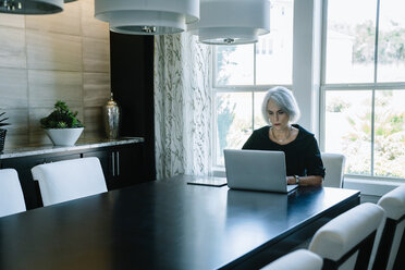 Geschäftsfrau arbeitet am Laptop, während sie im Büro am Fenster sitzt - CAVF25338