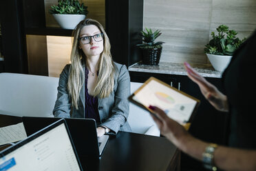 Businesswoman looking at female colleague discussing over tablet computer in office - CAVF25342