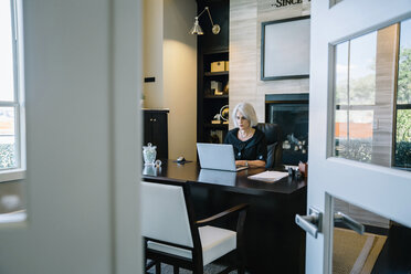 Geschäftsfrau arbeitet an Laptop-Computer am Schreibtisch im Büro durch die Tür gesehen - CAVF25349