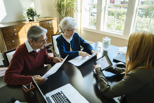 Blick von oben auf ein älteres Ehepaar, das Dokumente liest, während es mit einem Finanzberater im Büro diskutiert - CAVF25366