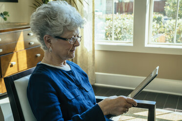 Senior woman using tablet computer while relaxing on chair at home - CAVF25378