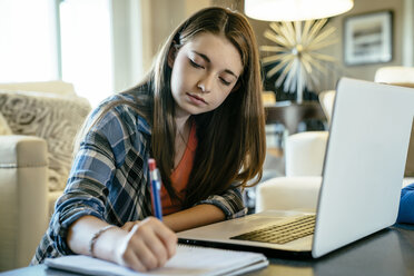 Serious teenage girl doing homework using laptop computer at home - CAVF25382