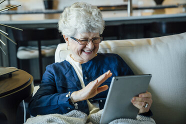 Glückliche ältere Frau bei einer Videokonferenz über einen Tablet-Computer, während sie sich auf dem Sofa zu Hause entspannt - CAVF25397