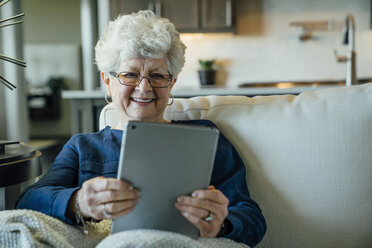 Ältere Frau lächelt, während sie einen Tablet-Computer auf dem Sofa zu Hause benutzt - CAVF25398