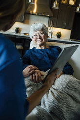 Ausgeschnittenes Bild einer Hauspflegerin, die einer älteren Frau im Wohnzimmer einen Tablet-Computer zeigt - CAVF25403