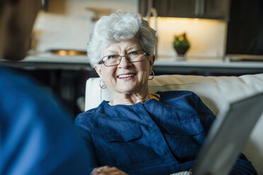 Happy senior woman looking at home caregiver in living room - CAVF25404