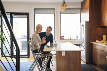 Senior couple discussing while sitting by laptop computer at home - CAVF25410