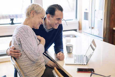 Lächelndes älteres Paar, das am Tisch sitzend auf einen Laptop-Computer schaut - CAVF25414