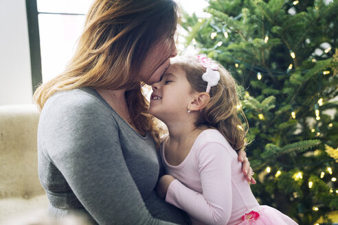 Nahaufnahme einer Mutter, die ihre Tochter zu Hause unter dem Weihnachtsbaum küsst - CAVF25422