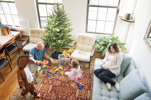 Hoher Blickwinkel auf einen Vater, der mit seinen Kindern spielt, während eine schwangere Frau auf dem Sofa sitzt - CAVF25425