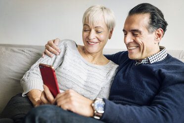 Älteres Paar schaut auf sein Smartphone, während es zu Hause auf dem Sofa sitzt - CAVF25432