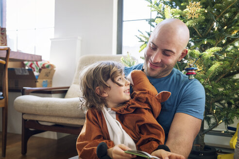 Happy father looking at son dressed in costume against Christmas tree at home - CAVF25438