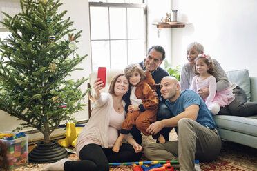 Schwangere Frau, die ein Selfie macht, während sie mit ihrer Familie unter dem Weihnachtsbaum zu Hause sitzt - CAVF25444