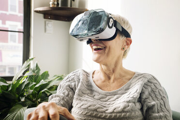 Glückliche ältere Frau, die einen Virtual-Reality-Simulator zu Hause an der Wand trägt - CAVF25451