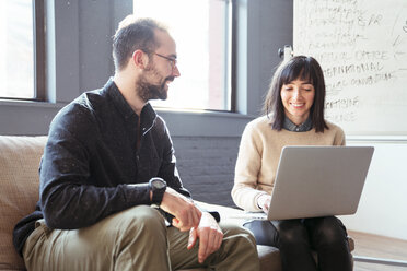 Man looking at businesswoman using laptop computer in office - CAVF25568