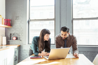 Man and woman using laptop computer while standing at table in office - CAVF25578