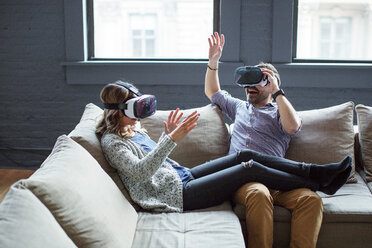 Colleagues wearing virtual reality simulators while sitting on sofa in office - CAVF25580