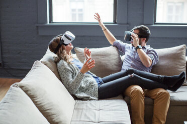 Coworkers wearing virtual reality simulators while sitting on sofa in office - CAVF25581