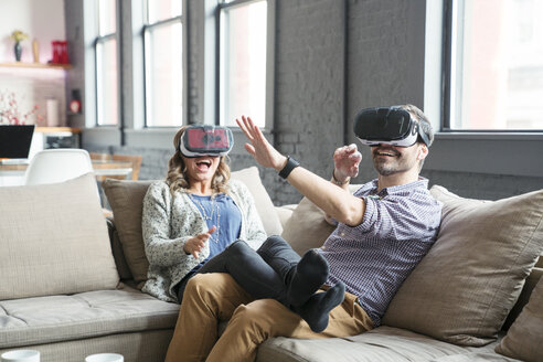 Kollegen tragen einen Virtual-Reality-Simulator, während sie auf dem Sofa im Büro sitzen - CAVF25598