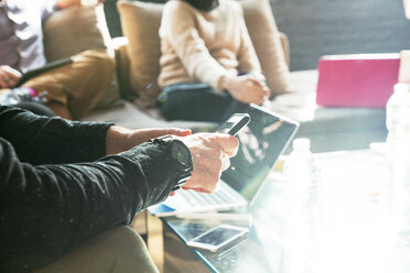 Ausgeschnittenes Bild eines Geschäftsmannes, der ein Smartphone benutzt, während er mit Kollegen im Büro sitzt - CAVF25607