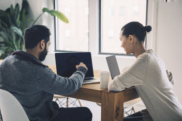 Businessman showing laptop computer to colleague while sitting at desk in office - CAVF25615